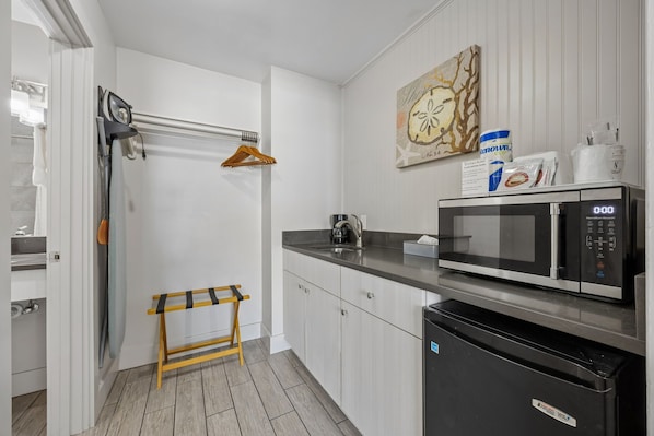 A modern kitchen with a microwave, a sink, and a wooden stool. - Beachside Motel (Fernandina Beach)