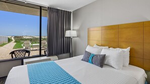 A hotel room with a large bed, a view of the beach, a window with curtains, and a headboard. - Beachside Motel (Fernandina Beach)