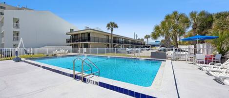 A swimming pool with a white fence, lounge chairs, and palm trees.