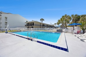A swimming pool with a white fence, lounge chairs, and palm trees. - Beachside Motel (Fernandina Beach)