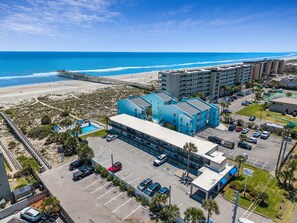 A coastal hotel with a parking lot, a beach, and a pier. - Beachside Motel (Fernandina Beach)