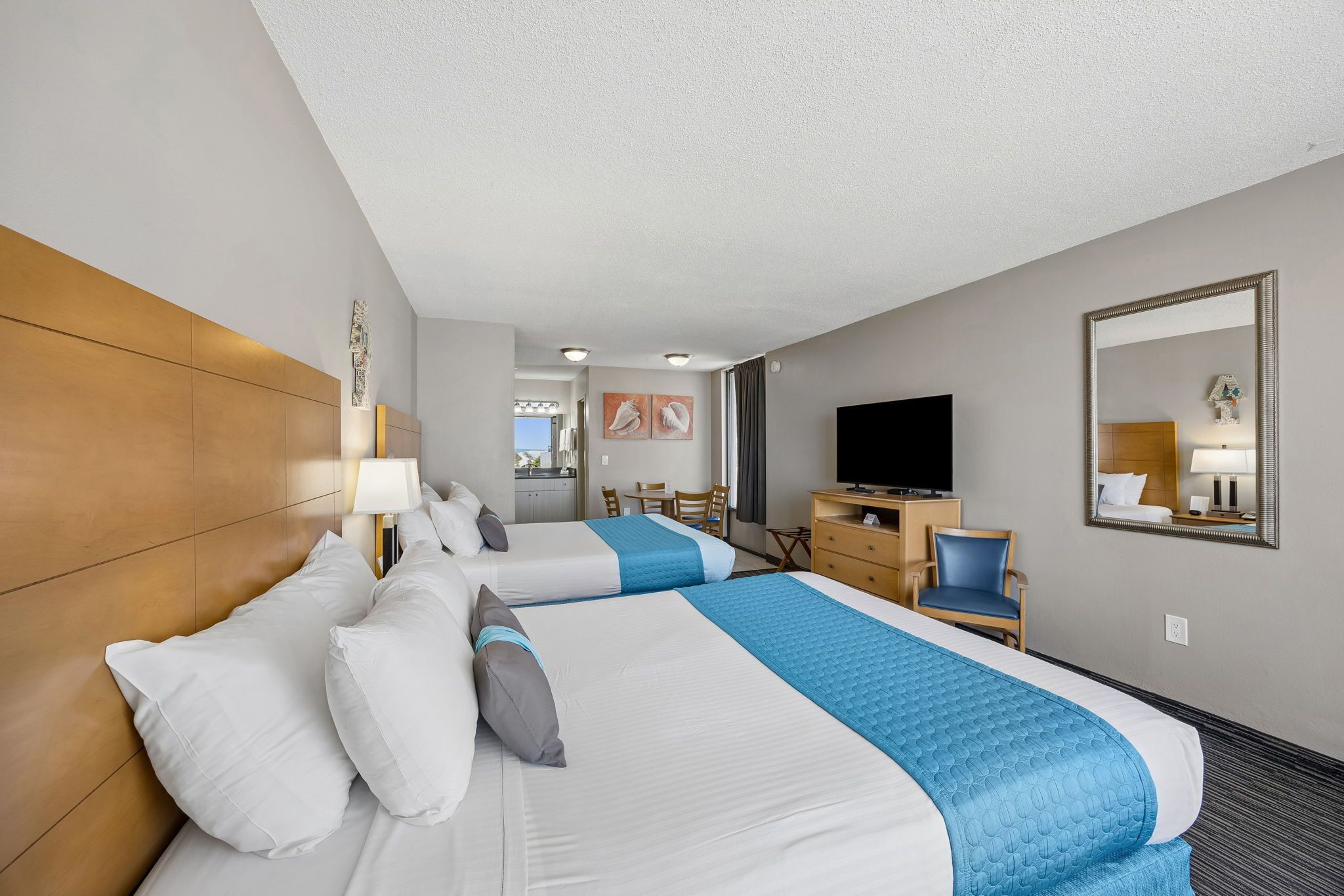 A hotel room with two beds, a TV, a desk, and a mirror.