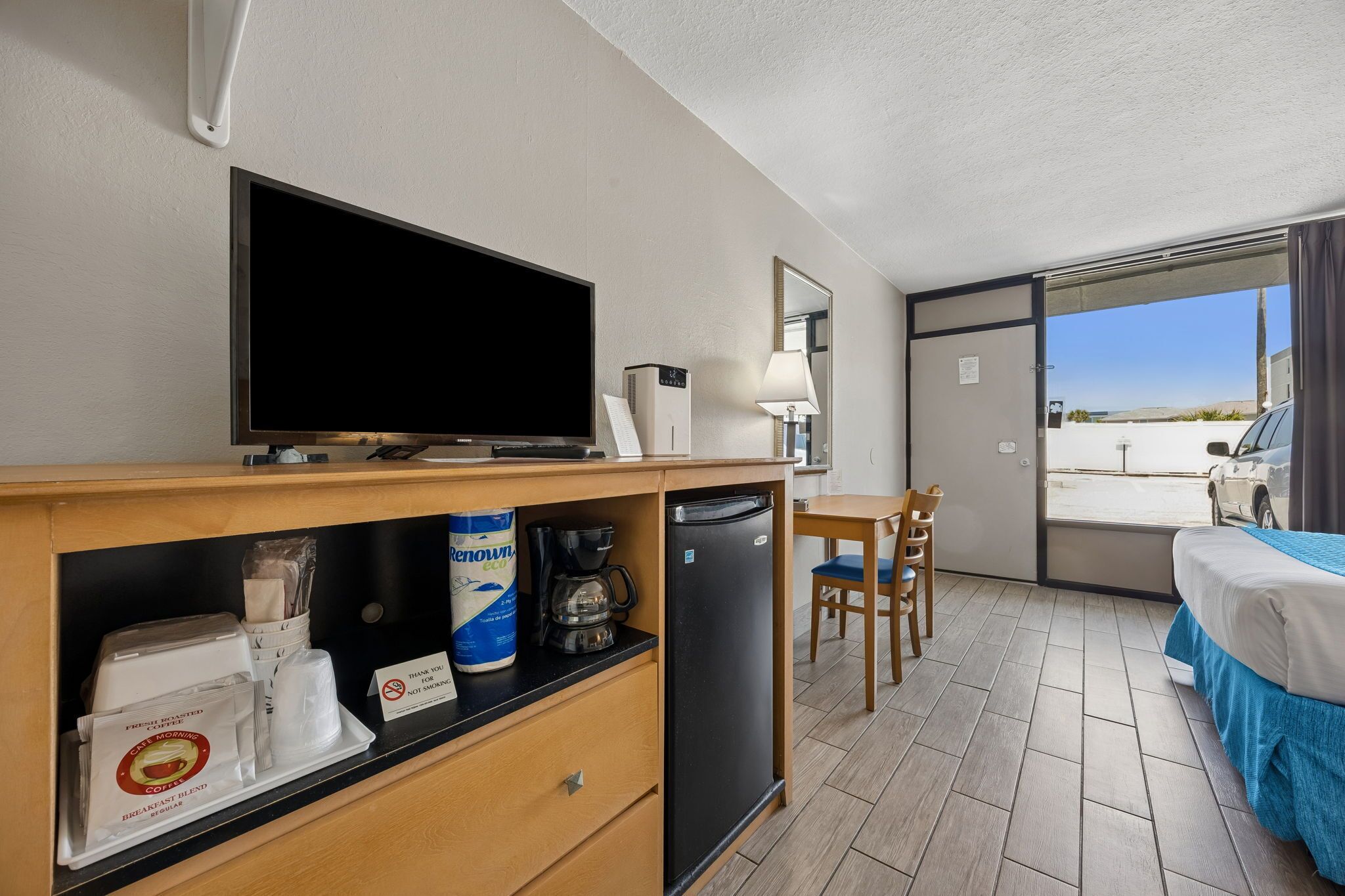 A hotel room with a TV, coffee maker, breakfast items, a desk, chair, and a bed.