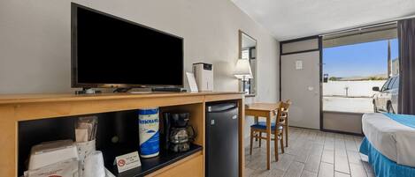 Een hotelkamer met televisie, koffiezetapparaat, ontbijtartikelen, bureau, stoel en bed.