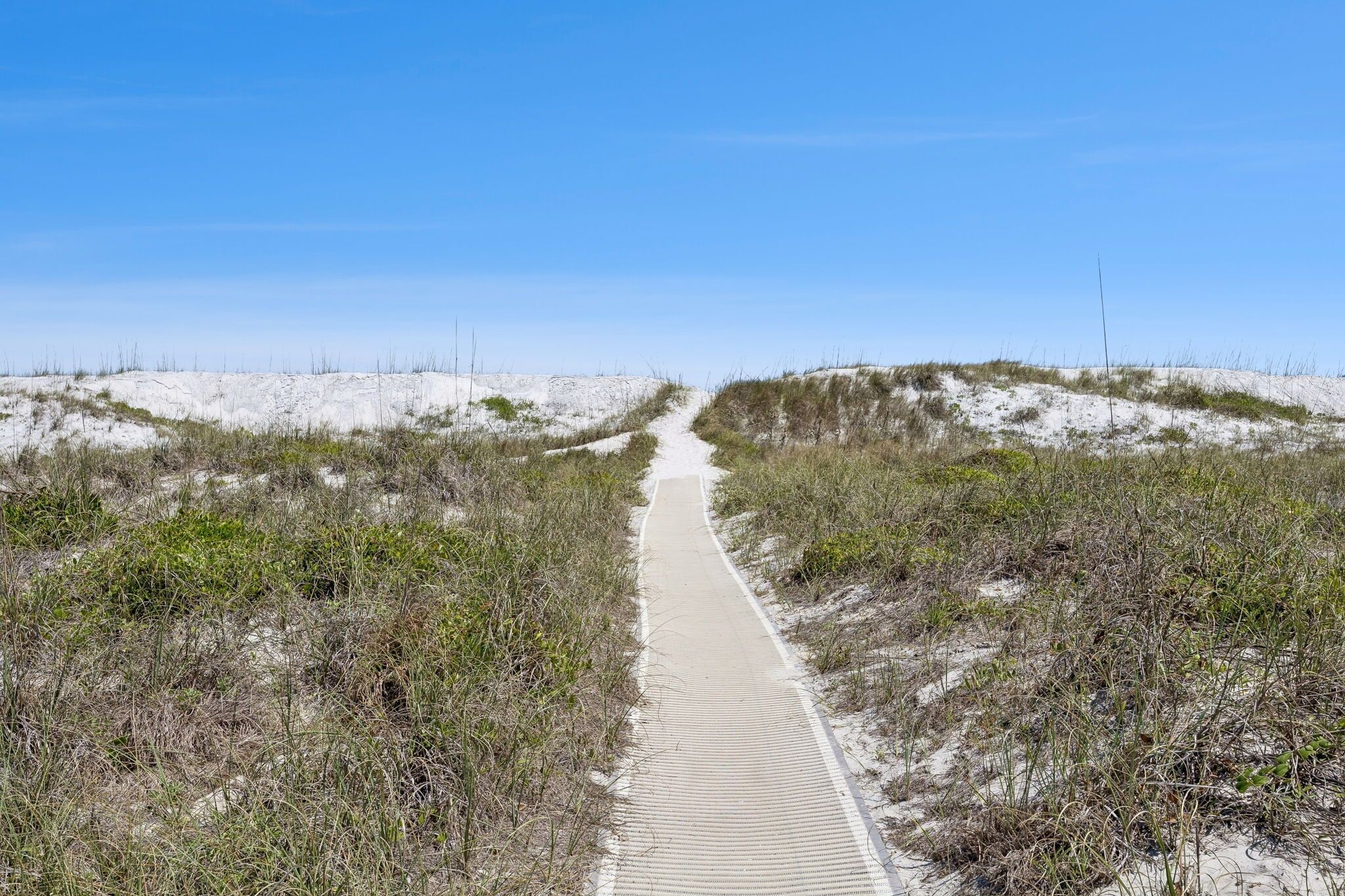 A sandy path flanked by dunes and sparse vegetation, leading into the distance.