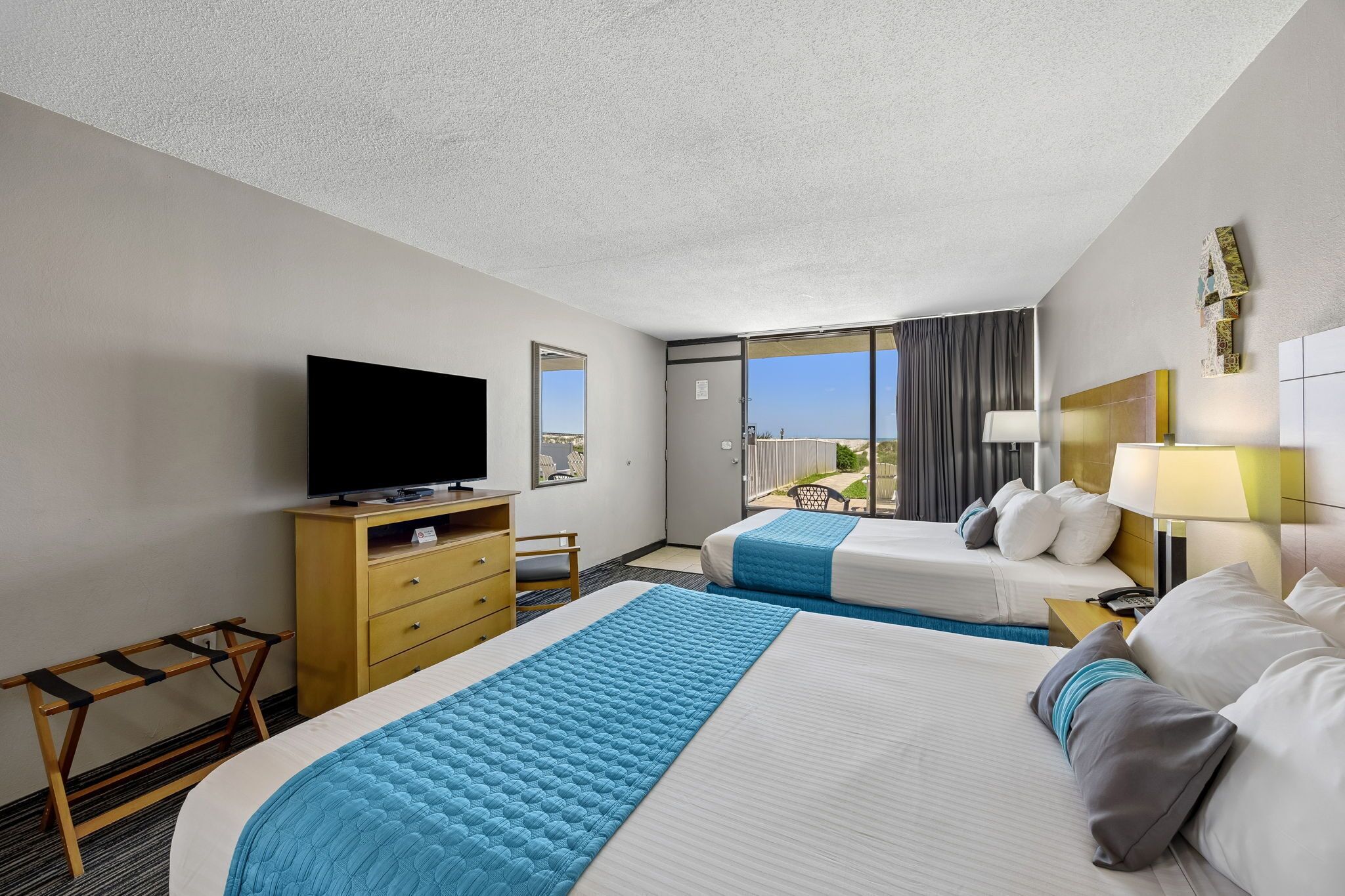 A hotel room with two beds, a television, a desk, and a window with a view.