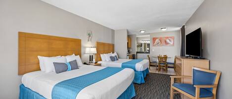 A hotel room with two beds, a desk, a chair, a television, and a kitchenette.