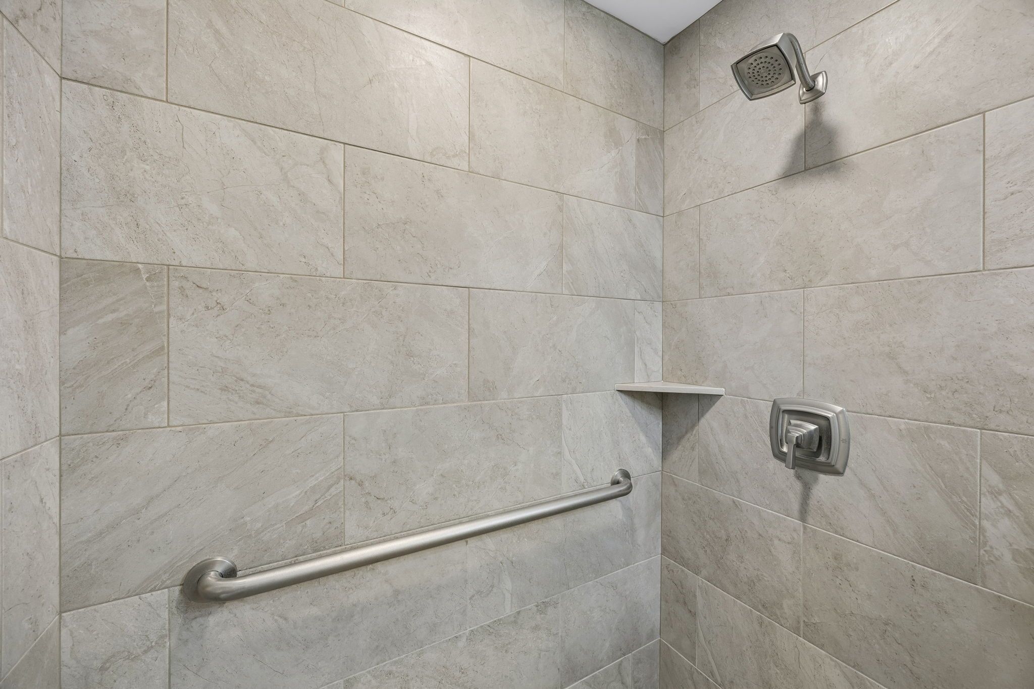 A shower with a handheld showerhead, a grab bar, and a wall-mounted control.