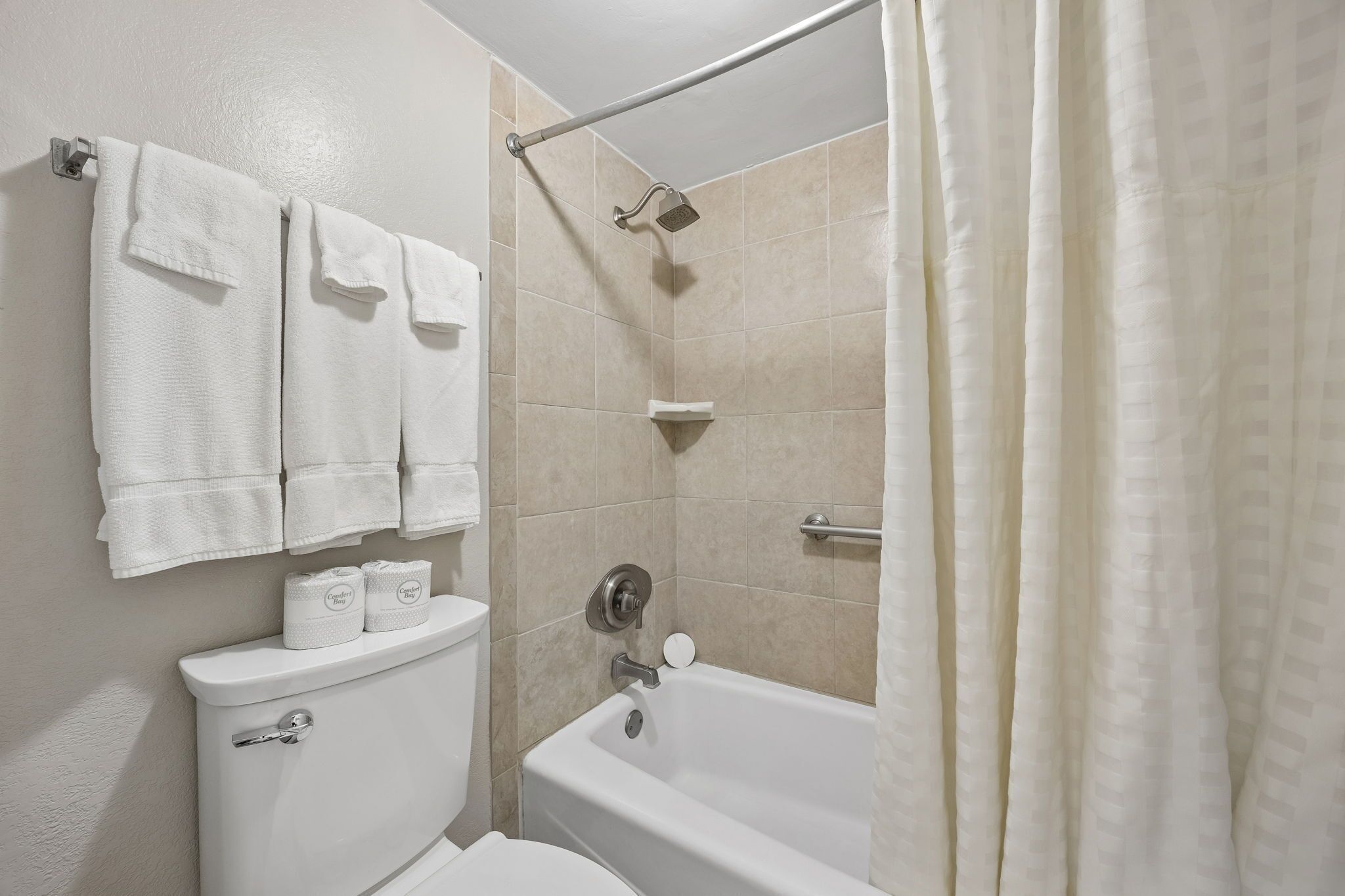A bathroom with a toilet, a bathtub, and a shower. There are towels hanging on the wall and a toilet paper holder.