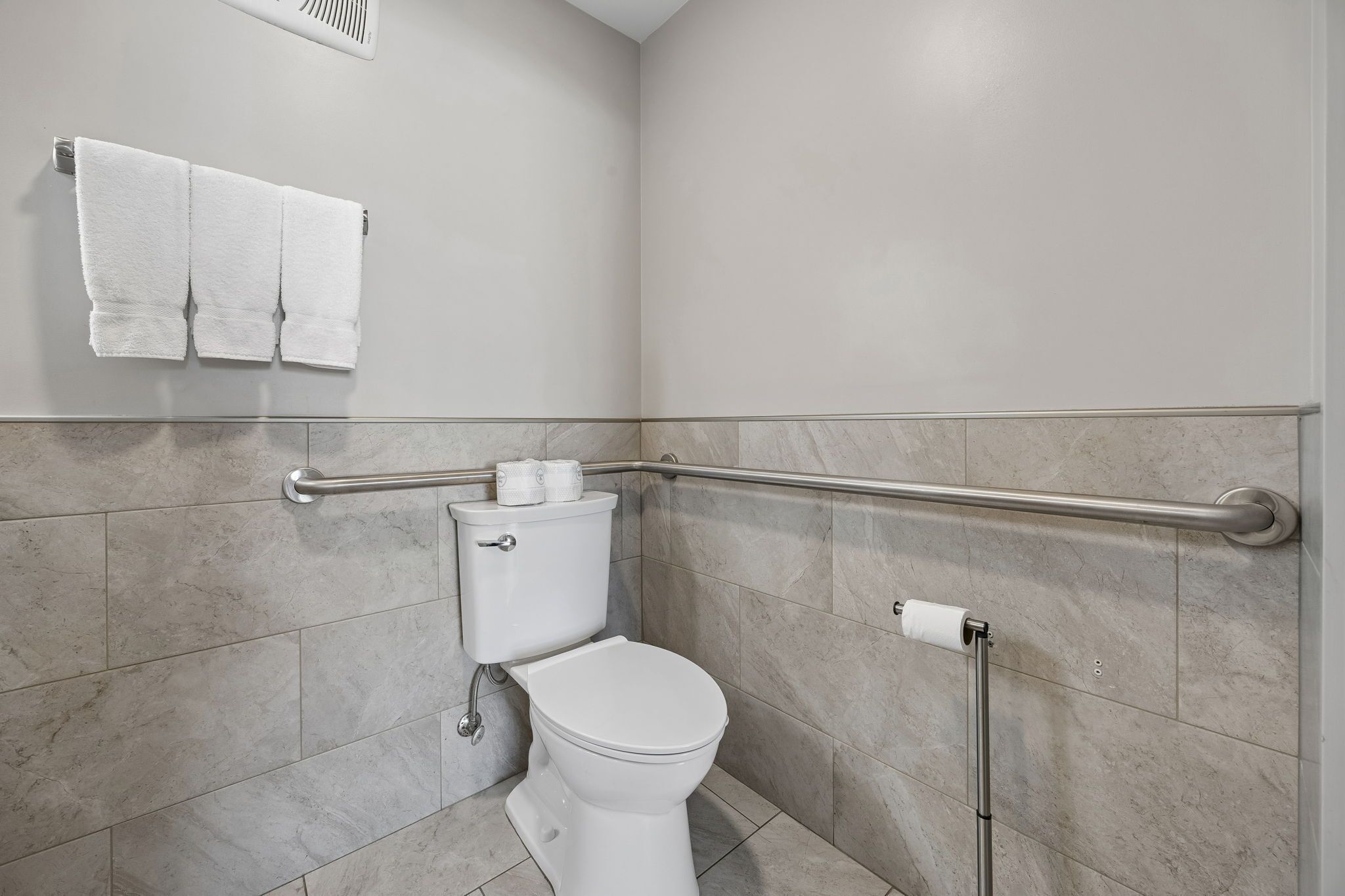 Une salle de bain équipée de toilettes, d’une barre d’appui et d’un porte-serviettes.