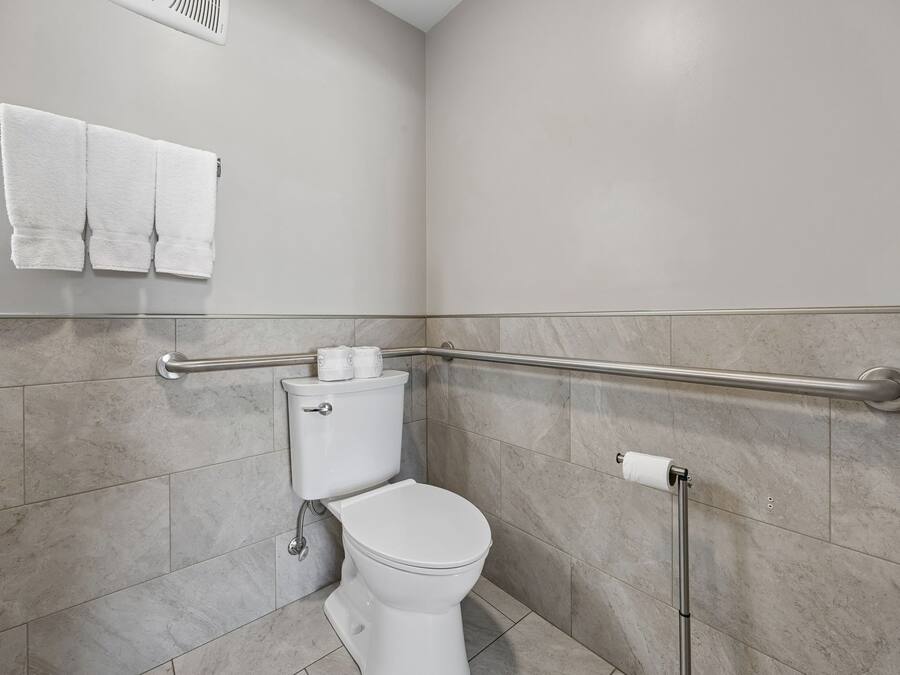 Une salle de bain équipée de toilettes, d’une barre d’appui et d’un porte-serviettes.