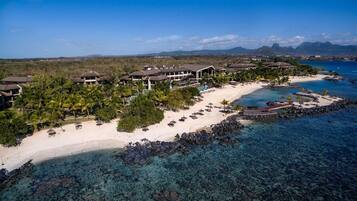An aerial view of a resort with multiple buildings, a sandy beach, and clear turquoise waters.