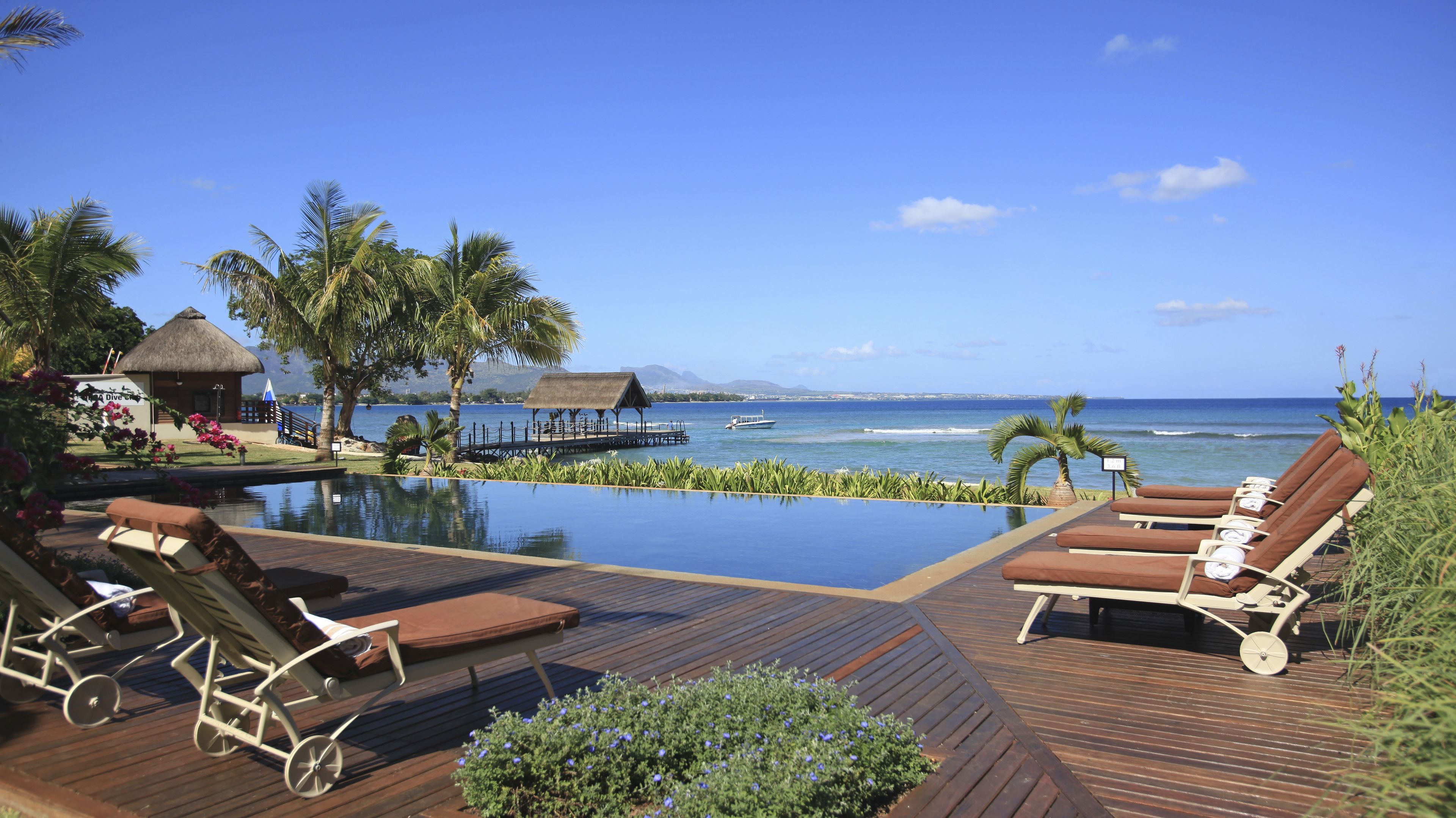An infinity pool with lounge chairs, a thatched-roof structure, and a view of the ocean.