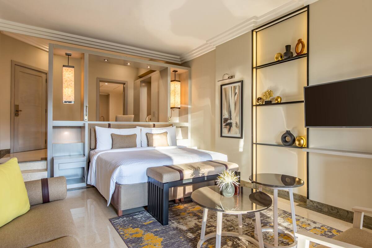 A modern hotel room with a large bed, a small table, a sofa, and a TV.