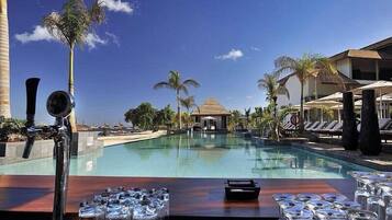Un bar junto a la piscina con vista a una alberca, palmeras y un edificio al fondo.