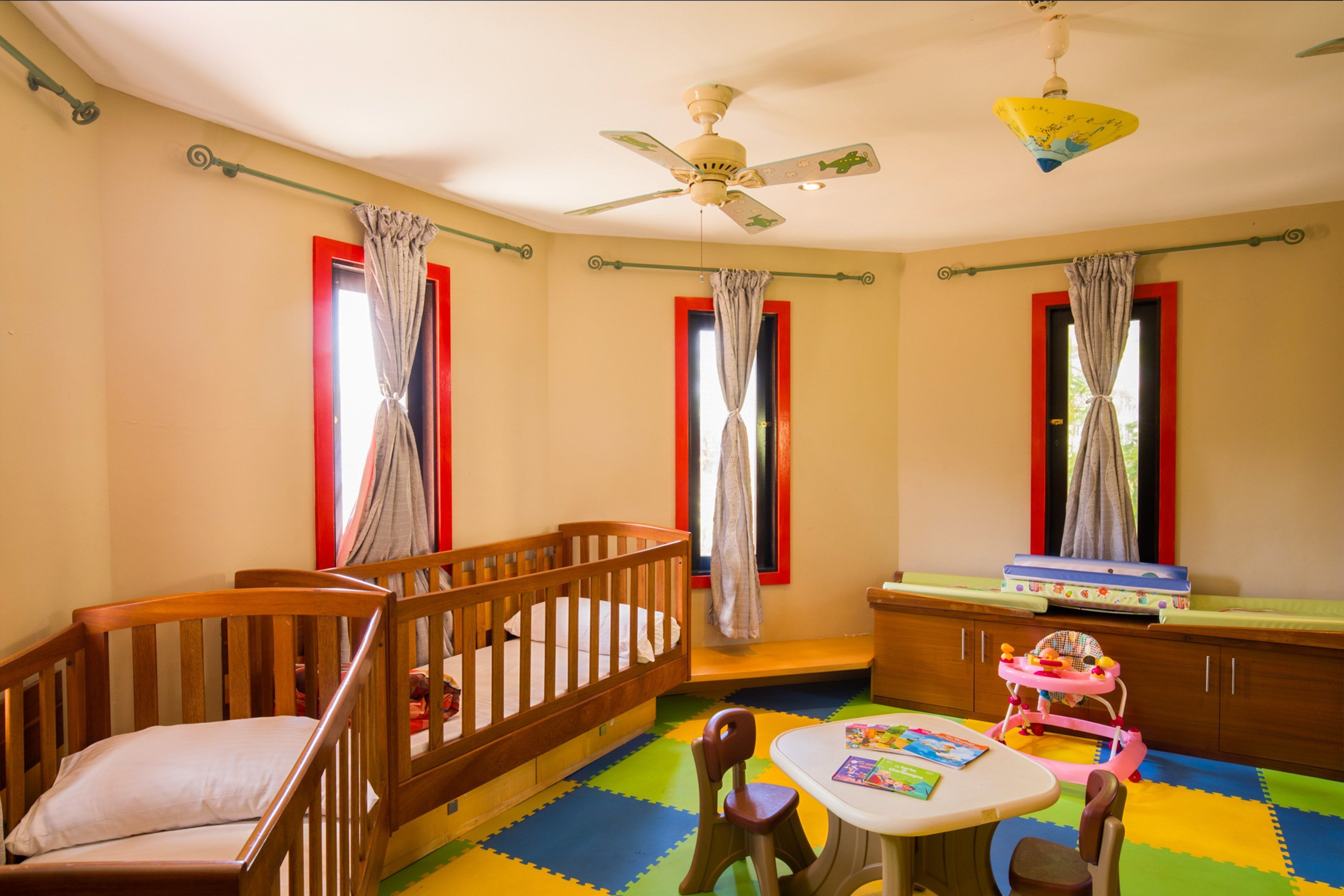 Une chambre d’enfant avec un berceau, une petite table avec des jouets et un ventilateur de plafond.
