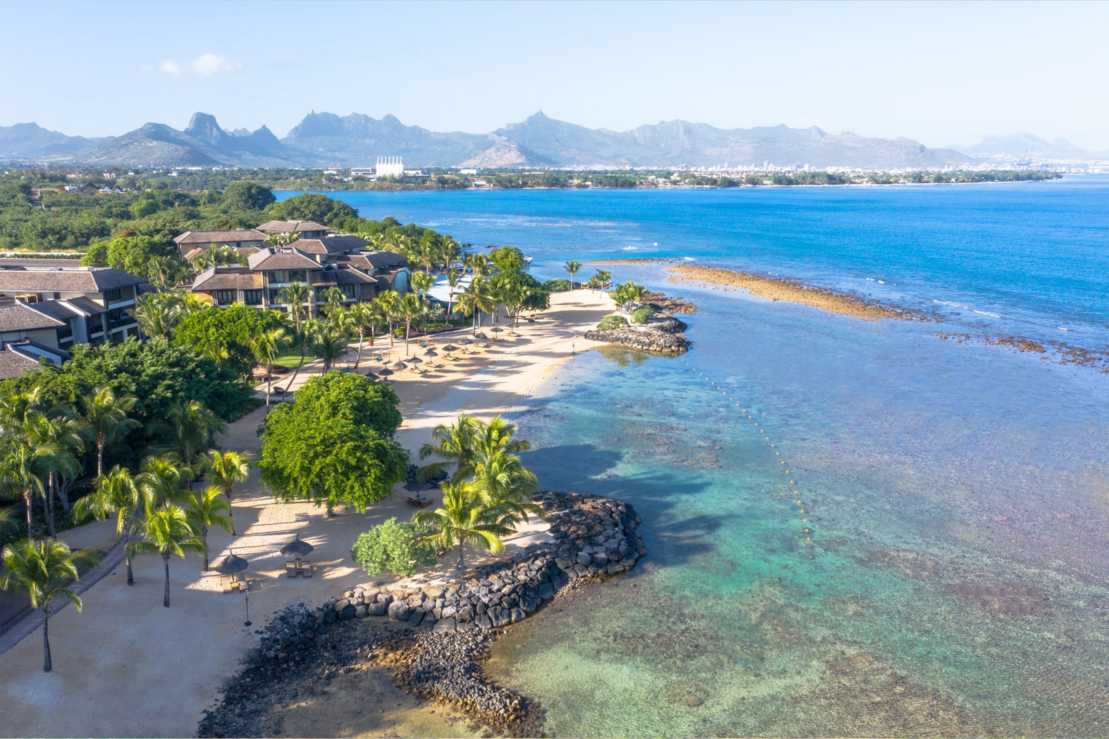 A resort with beachfront villas, palm trees, and clear blue waters.