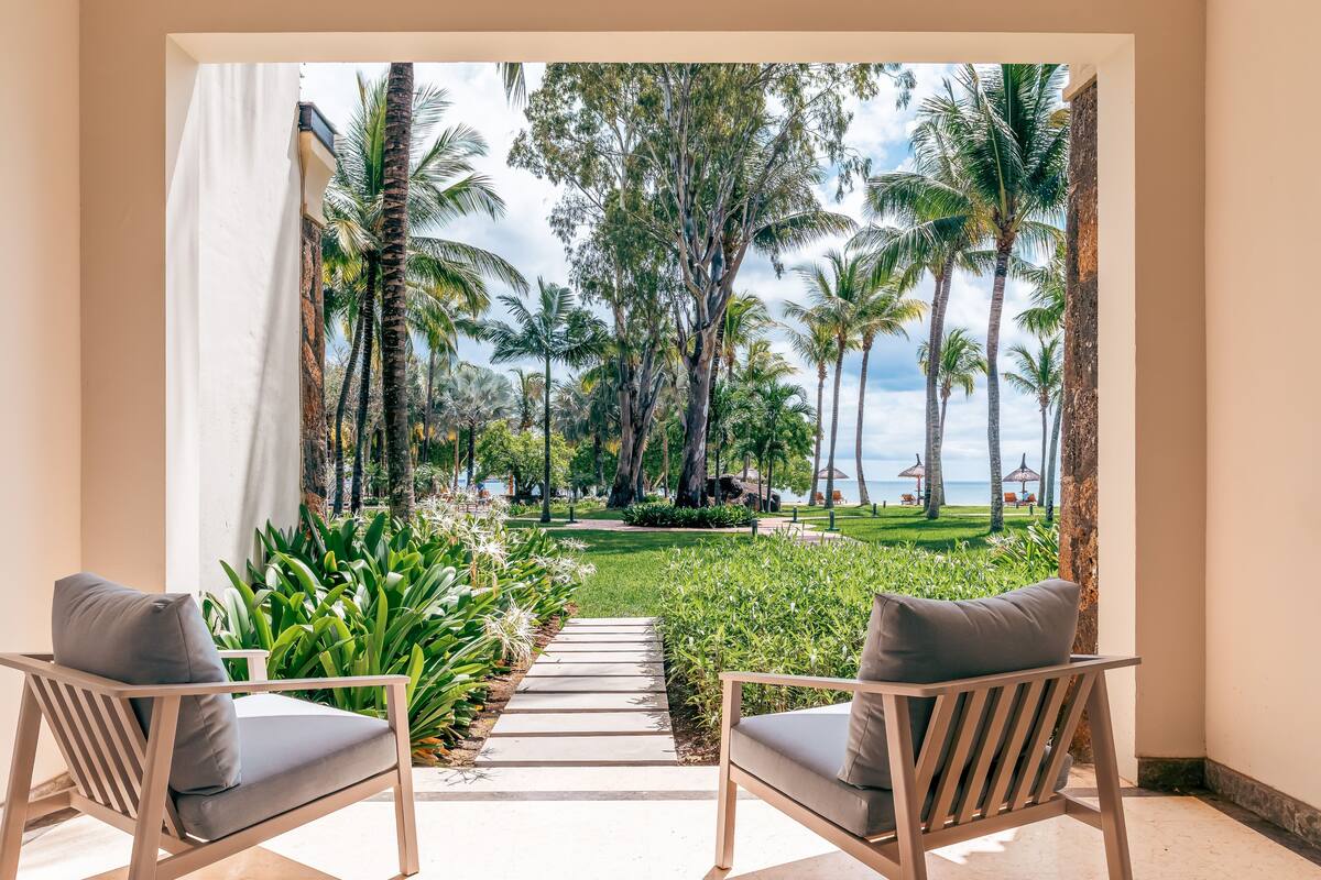A room with two chairs facing a view of a tropical garden and palm trees.