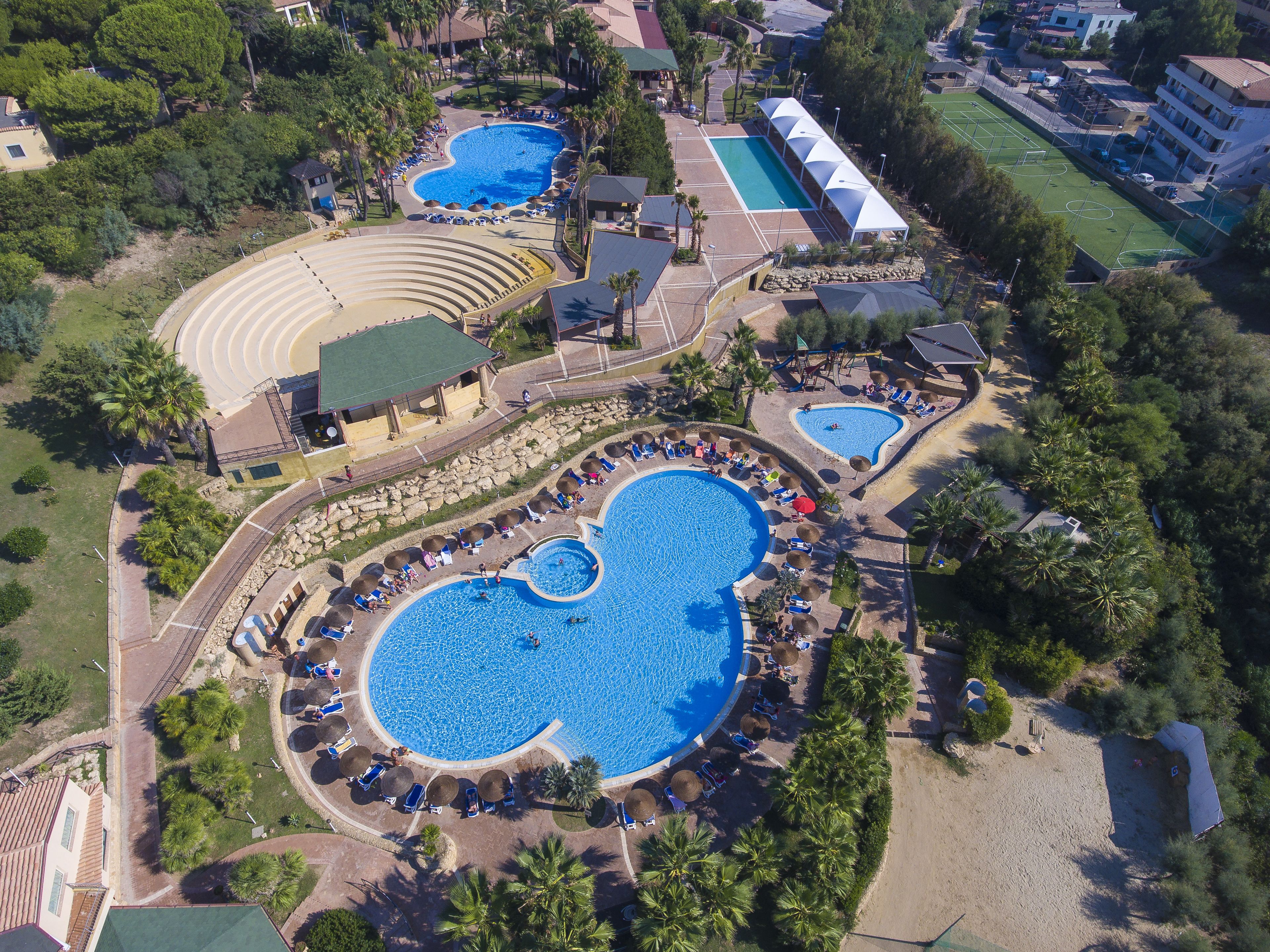 An aerial view of a resort with multiple swimming pools, a tennis court, and a beach area.