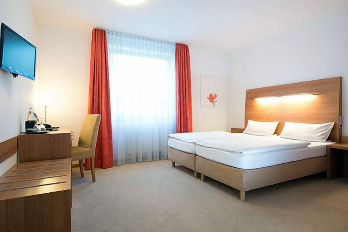 Hotellihuone, jossa on sänky, työpöytä, tuoli, televisio ja ikkuna, jossa on verhot.