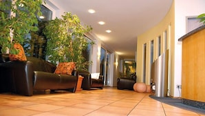 A spacious lobby with a modern design, featuring leather sofas, a large potted plant, and a tiled floor. - Hotel Lemp (Cologne)