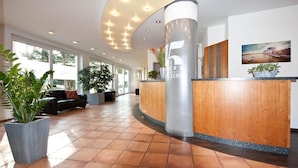 A modern reception area with a curved reception desk, large windows, and indoor plants. - Hotel Lemp (Cologne)