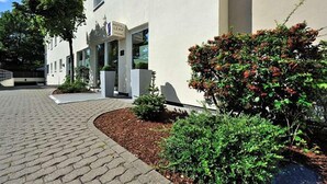 A hotel entrance with a paved driveway, a signboard, and well-maintained landscaping. - Hotel Lemp (Cologne)