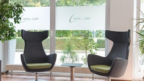 Two modern armchairs with green cushions in a bright room with large windows, a small table, and a sign reading "HOTEL LEMP". - Hotel Lemp (Cologne)