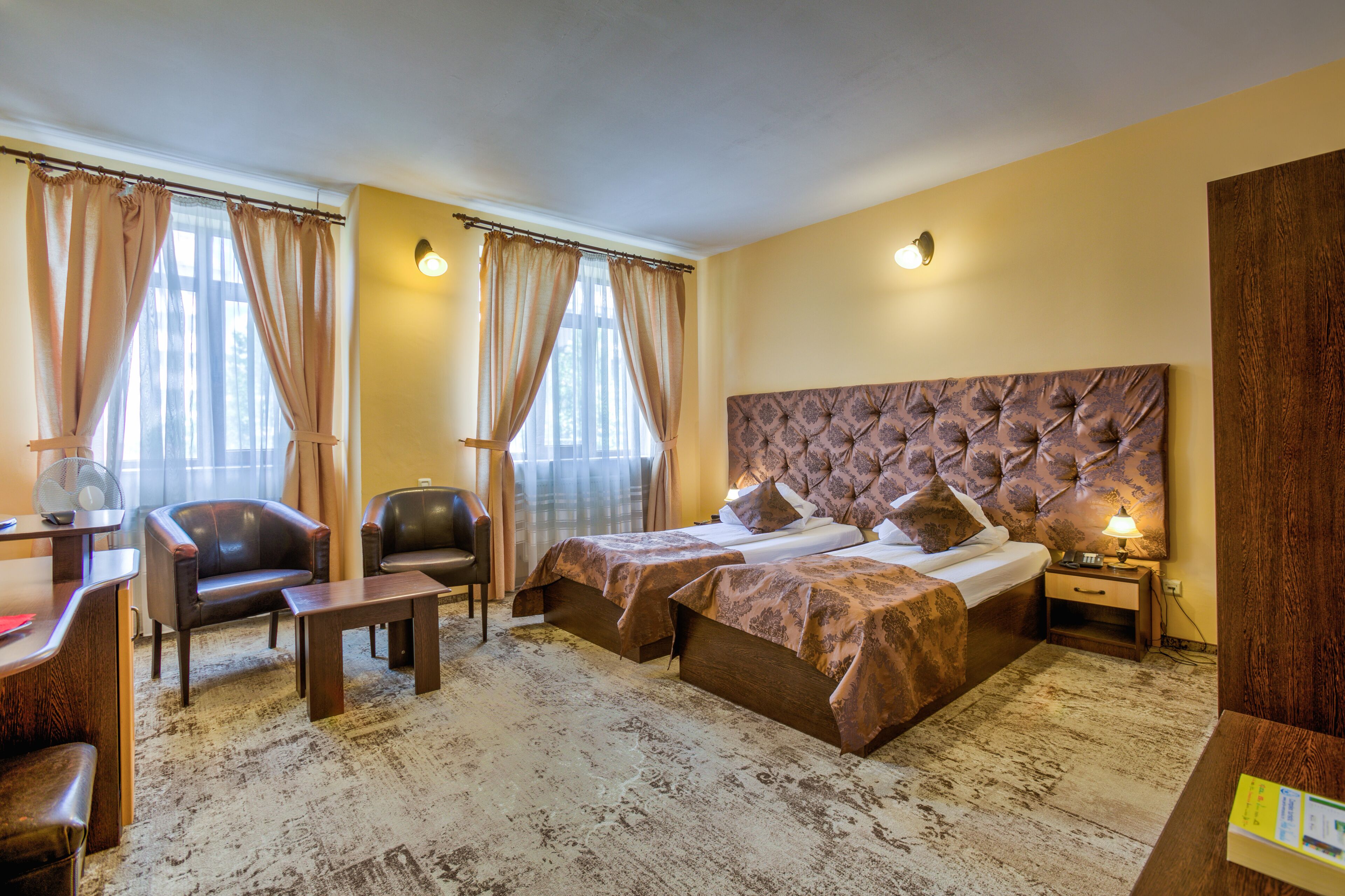 Una habitación de hotel con una cama grande, un escritorio con una silla, una mesita pequeña y una mesita de noche con una lámpara.