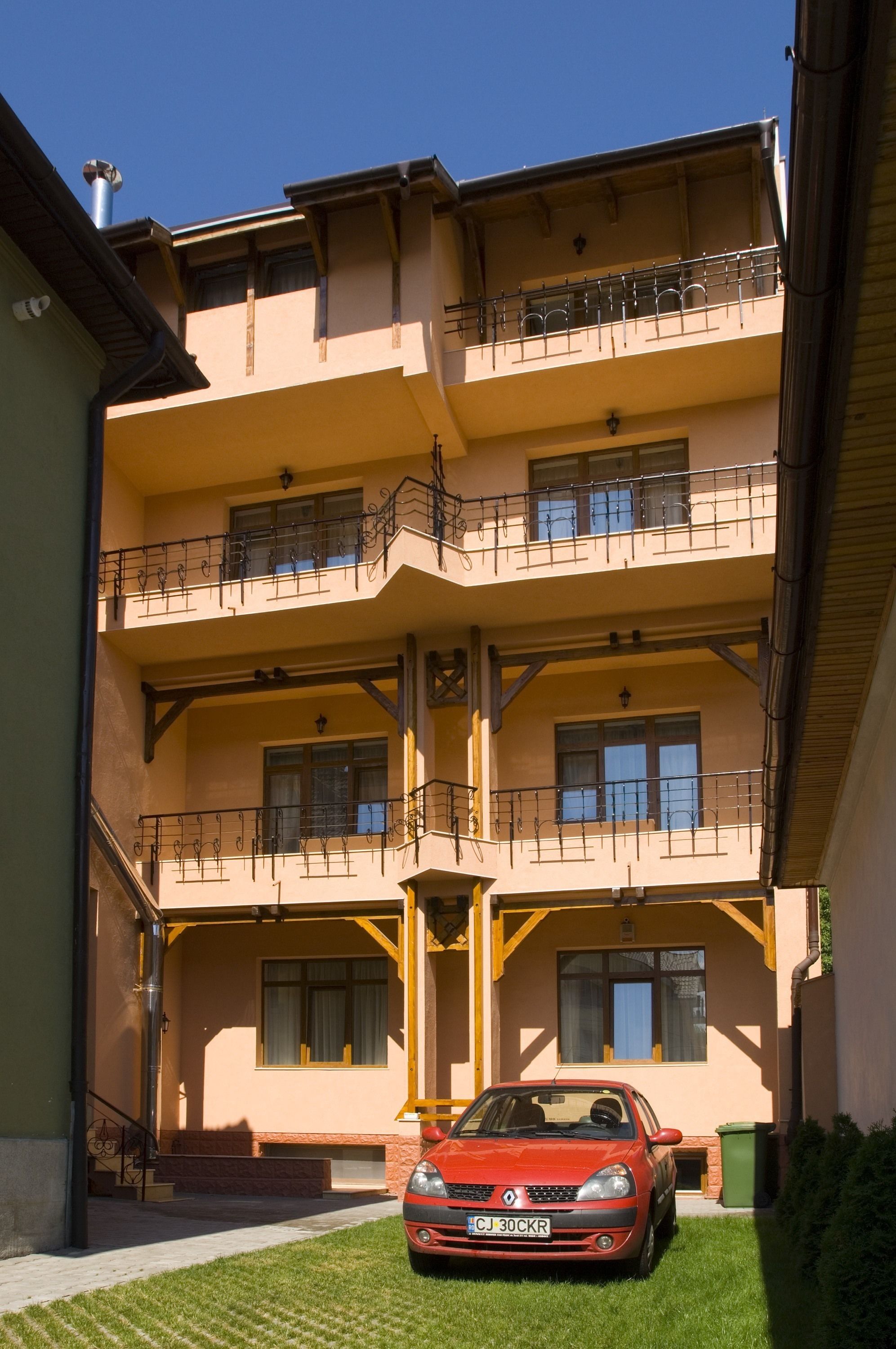 Un edificio de varios pisos con balcones, un auto rojo estacionado adelante y un cielo despejado.