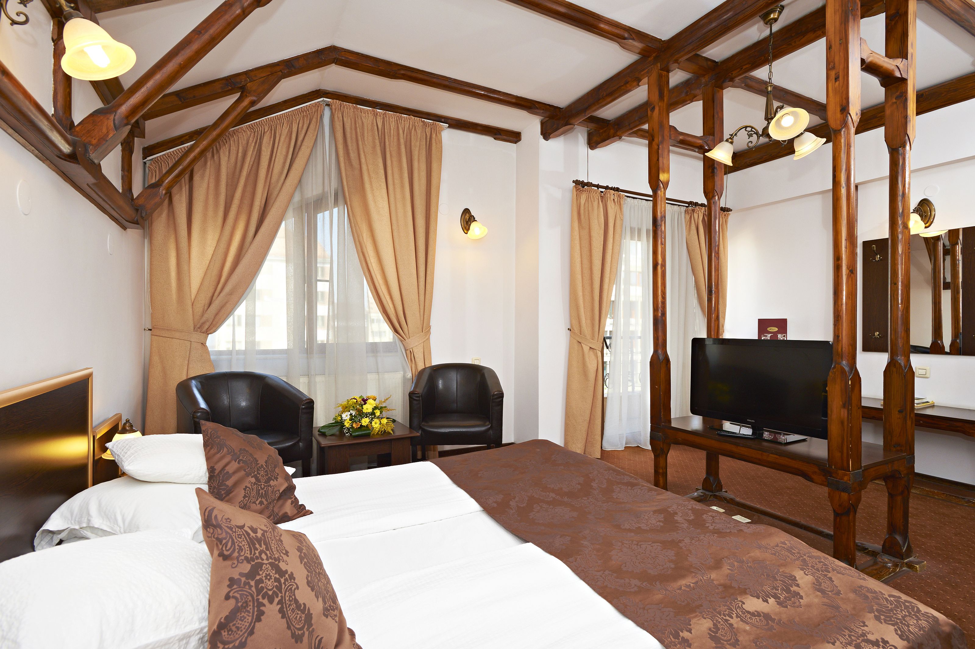 Habitación de hotel con una cama grande, dos sillas, un televisor y vigas de madera en el techo.