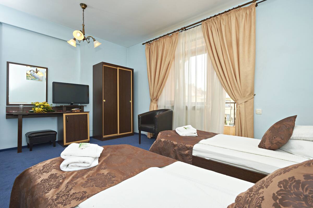 Habitación de hotel con dos camas, un escritorio con televisor, un armario y una silla.