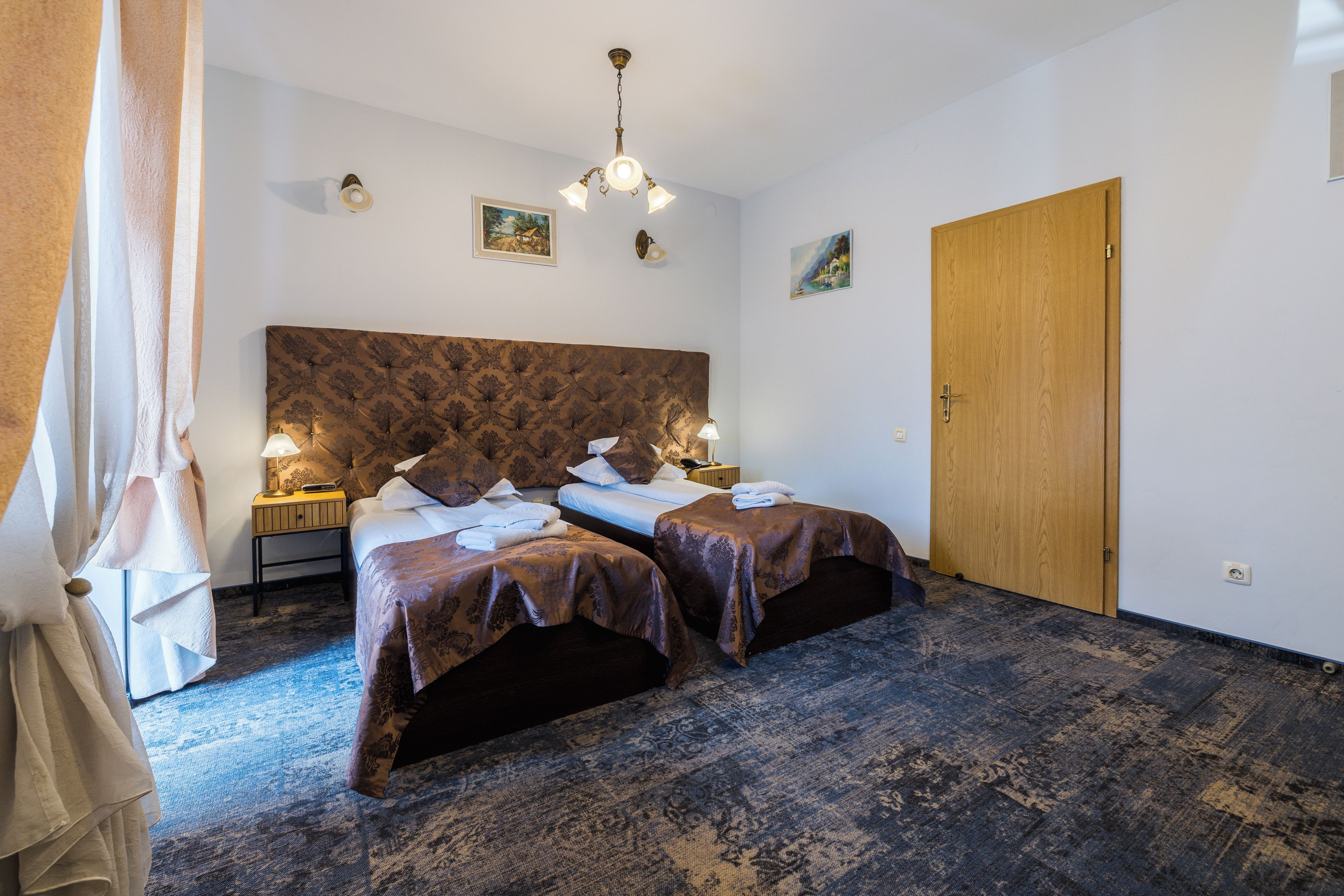 A hotel room with two beds, a wooden door, a patterned headboard, and a ceiling light fixture.