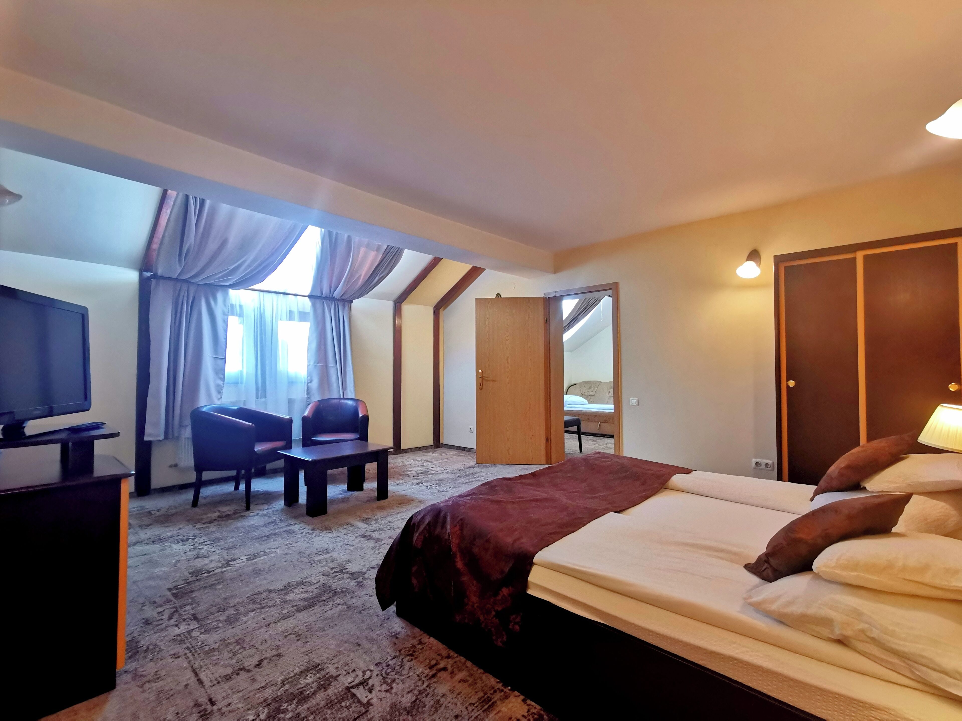 A hotel room with a bed, a desk with a computer, a chair, a TV, and a window with curtains.