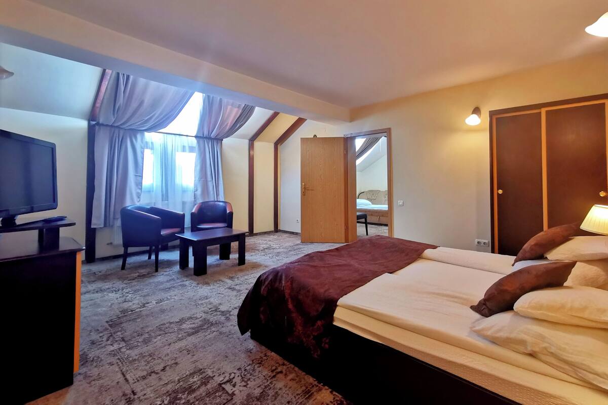 Habitación de hotel con cama, escritorio con computadora, silla, televisor y ventana con cortinas.