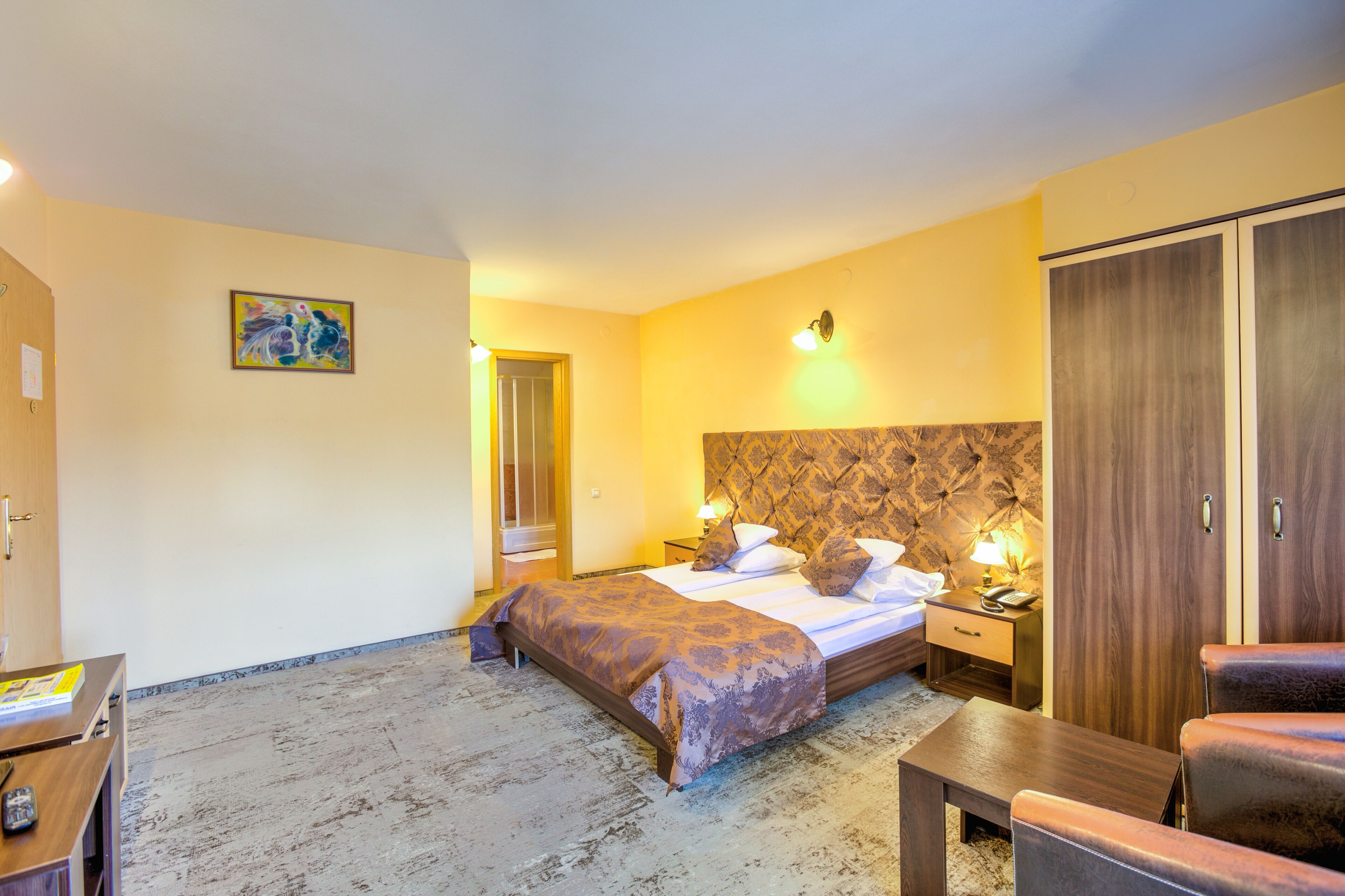 Una habitación de hotel con cama, mesita de noche, lámpara, armario y un cuadro en la pared.