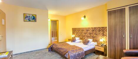 Una habitación de hotel con cama, mesita de noche, lámpara, armario y un cuadro en la pared.