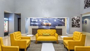 A lobby with a yellow sofa, two armchairs, a coffee table, and a wall mural of a racing car. - La Quinta Inn & Suites by Wyndham Sebring (Sebring)