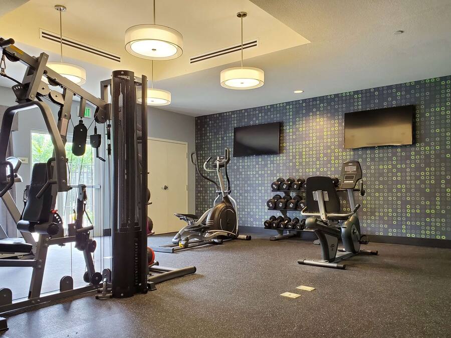 A gym with various exercise equipment, a wall-mounted TV, and a patterned wall.