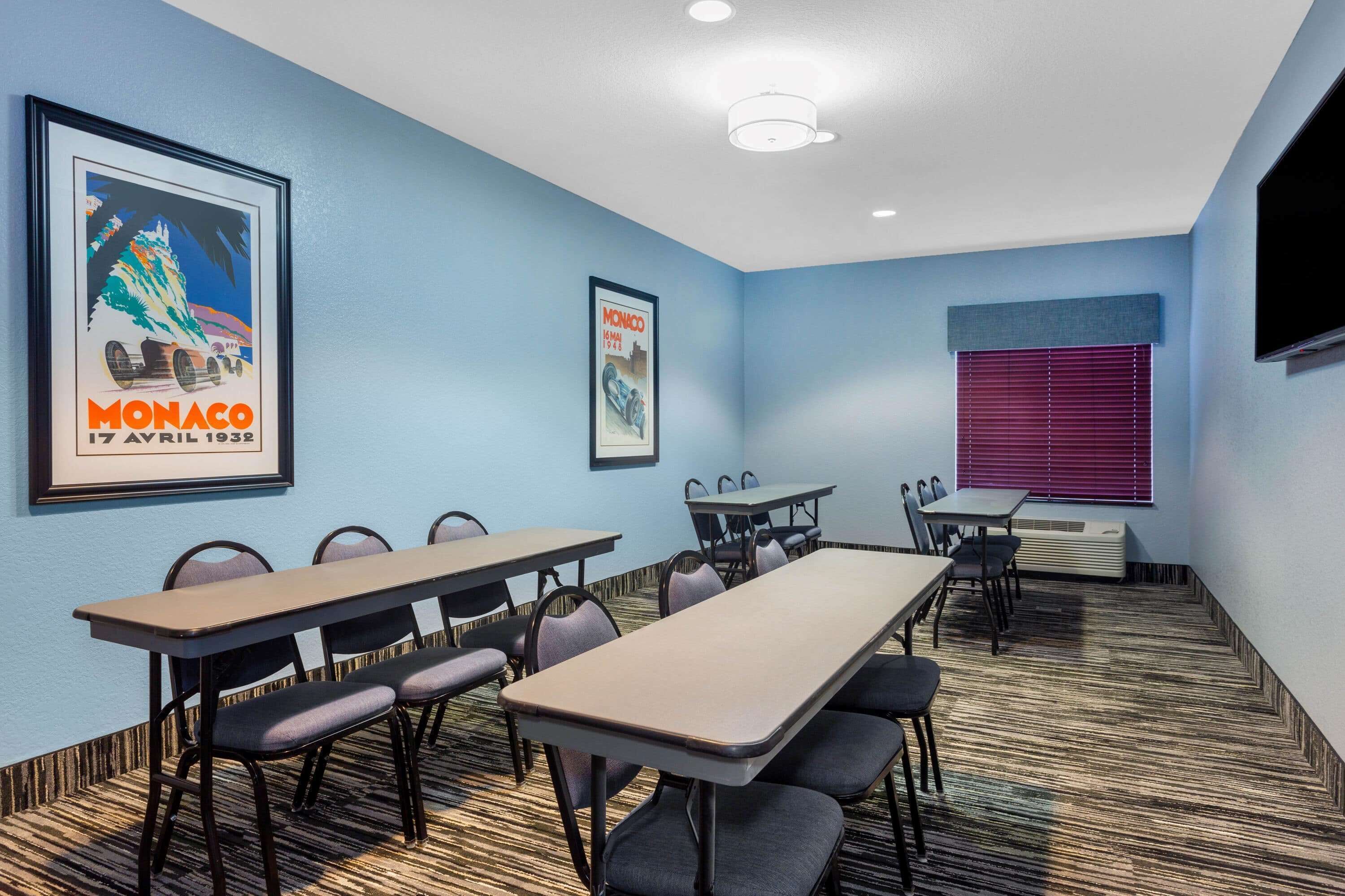 A conference room with tables and chairs, a large poster on the wall, and a window with blinds.