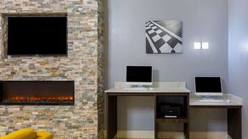A modern living room with a stone fireplace, two desks with computers, a flat-screen TV, and a yellow armchair.