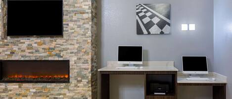 A modern living room with a stone fireplace, two desks with computers, a flat-screen TV, and a yellow armchair.