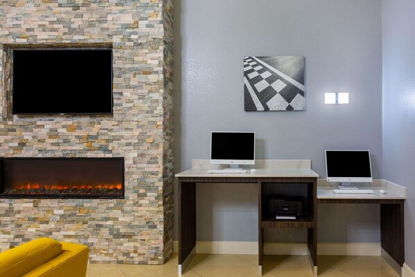 A modern living room with a stone fireplace, two desks with computers, a flat-screen TV, and a yellow armchair. - La Quinta Inn & Suites by Wyndham Sebring (Sebring)