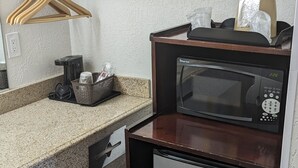A compact kitchenette with a stainless steel refrigerator, a microwave, and a wooden countertop. - Hillcrest Inn & Suites (Ozona)
