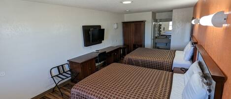 Habitación de hotel con dos camas, un escritorio, una silla, televisión y baño visible a través de una puerta abierta.