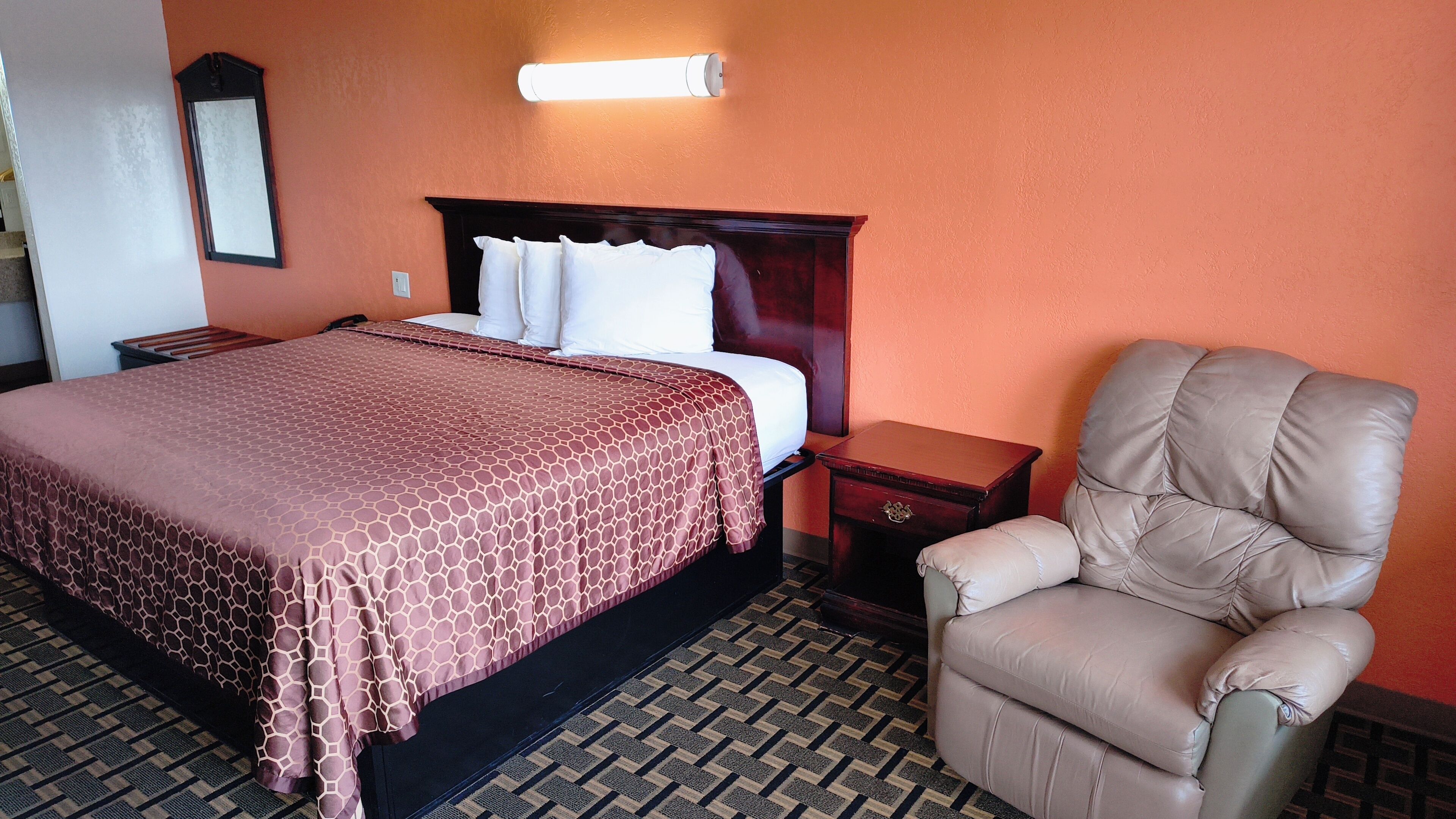 Una habitación de hotel con cama, una silla, una mesita de noche y una lámpara fijada a la pared.