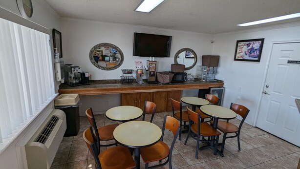 A small, clean cafe with a counter, several tables, and chairs. There are coffee machines, a TV, and a door marked "Employees Only". - Hillcrest Inn & Suites (Ozona)