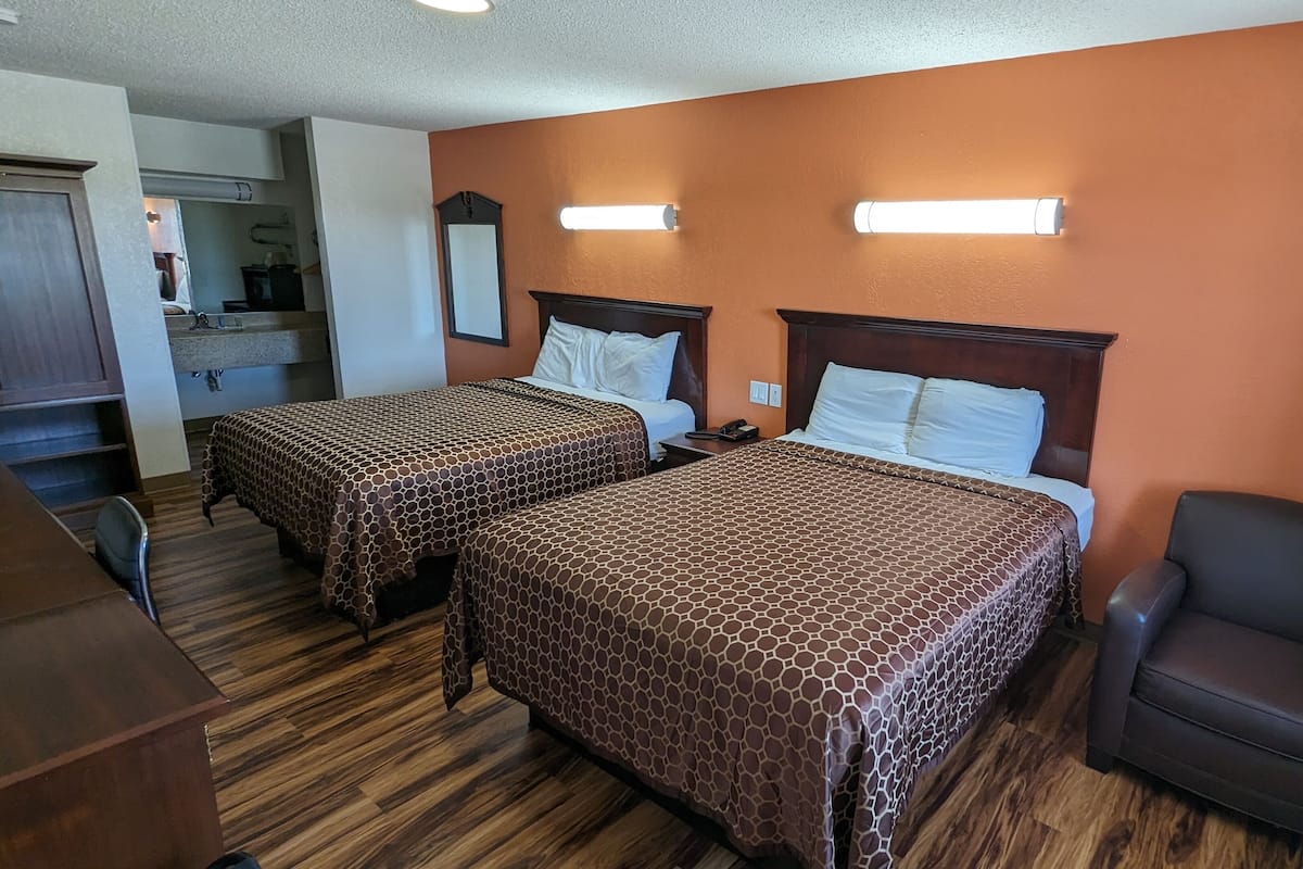 Une chambre d’hôtel avec deux lits, un bureau, une chaise et une salle de bain visible au fond.