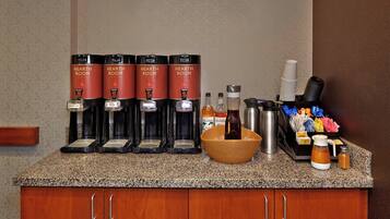 A coffee station with four branded dispensers, a bowl with a bottle, and various condiments and utensils.