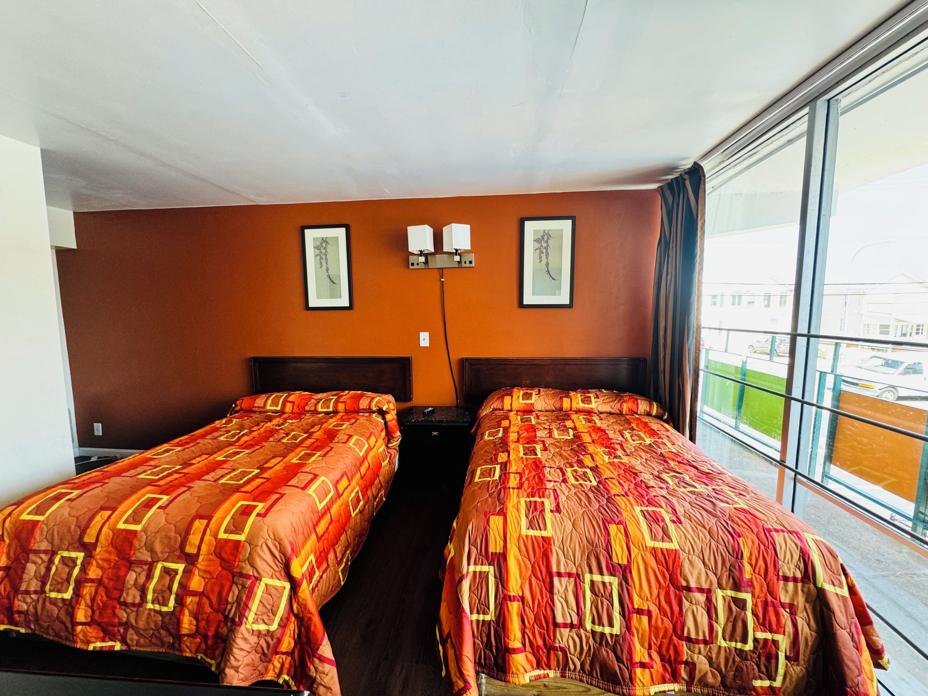 Habitación de hotel con dos camas, cada una con colcha estampada, una mesita de noche, una lámpara de pared y una ventana con vistas al exterior.